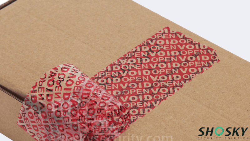 Red tamper-evident carton sealing tape peeled back from a cardboard package to leave a clear "VOID OPEN" pattern residue.