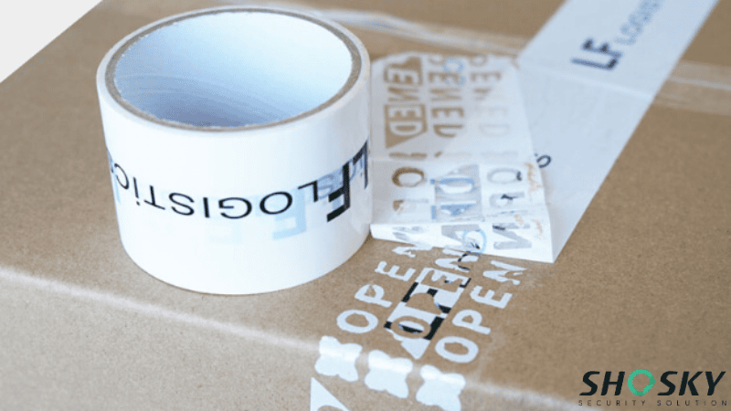 A roll of white custom-printed carton sealing tape placed on a box alongside a peeled strip revealing "OPENED" tamper-evident text.