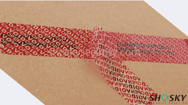 Red tamper-evident carton sealing tape being peeled back from cardboard to reveal a bold "VOID OPEN" hidden security message.