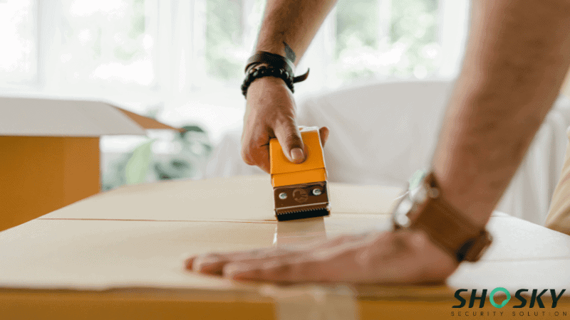 ALT: A person using a yellow handheld carton sealing tape dispenser to seal a cardboard shipping box.