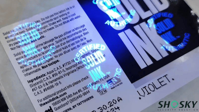Etiqueta de segurança em um frasco de tinta para tatuagem com marcas de autenticação de tinta UV que brilham sob luz negra.