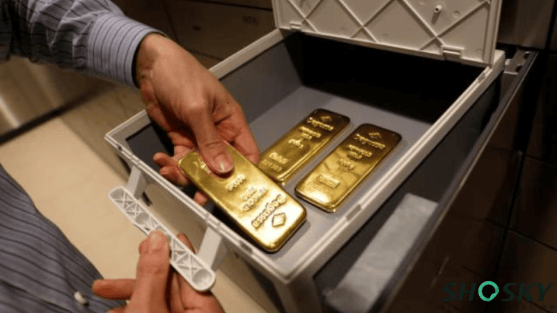Hands placing gold bullion bars into a high-security vault storage box.