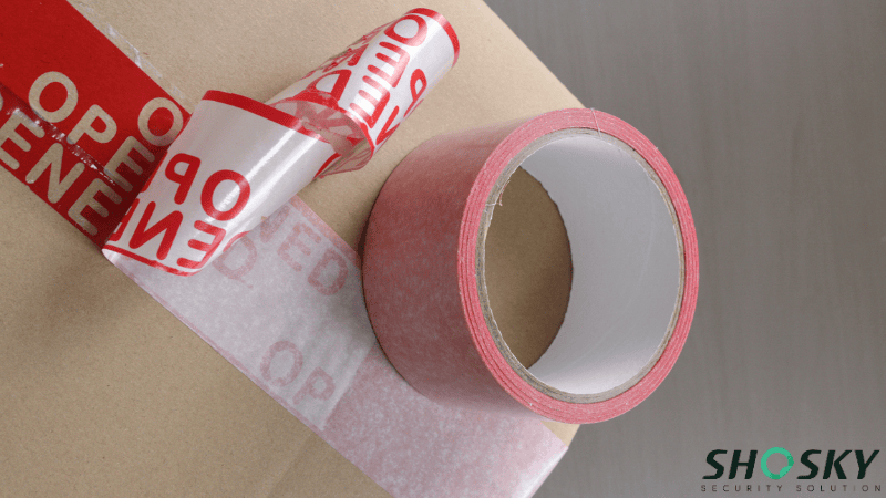 A roll of red paper void tape on a cardboard box, with a peeled section revealing the "OPENED" message.