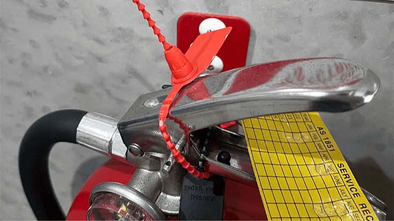 Red plastic pull-tight tamper seal securing the safety pin on a fire extinguisher handle.