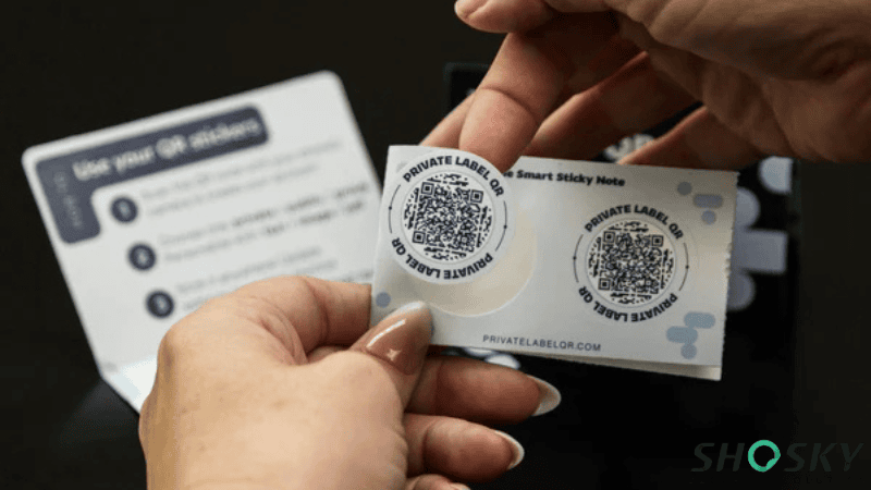 A person peeling a round QR code security label printed with "PRIVATE LABEL QR" text off a backing sheet.