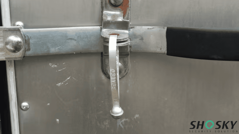 A silver metal strap seal stamped with the word "SEALED" locked onto the latch mechanism of a cargo door.
