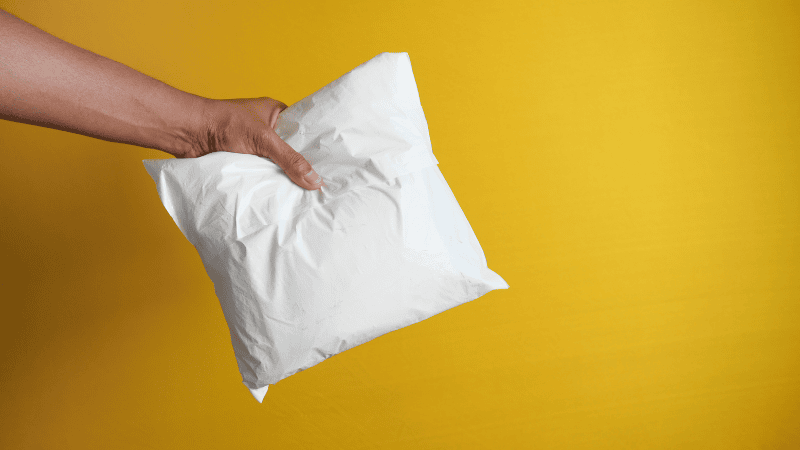 a man hand a white poly mailer in front of the yellow wall