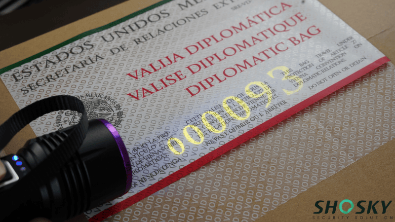 A UV flashlight shining on a diplomatic bag seal made of tamper evident material, illuminating a hidden serial number printed in fluorescent uv ink.