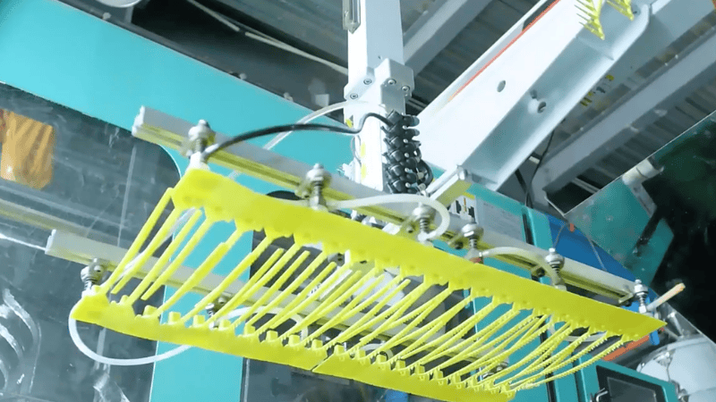 Automated industrial robotic arm manufacturing a set of yellow fixed-length plastic security seals in a factory setting.