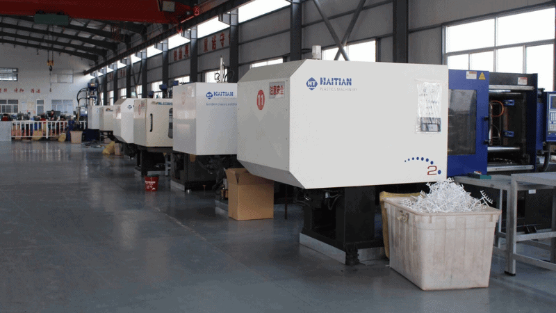 A row of Haitian plastic injection molding machines operating in a factory workshop with plastic seals gathered in a container.