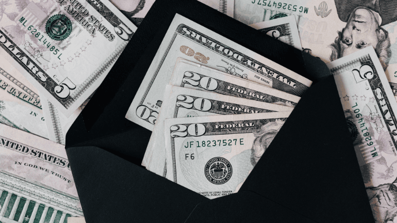 A black envelope filled with twenty-dollar US bills surrounded by cash, representing effective cash management and secure currency handling.