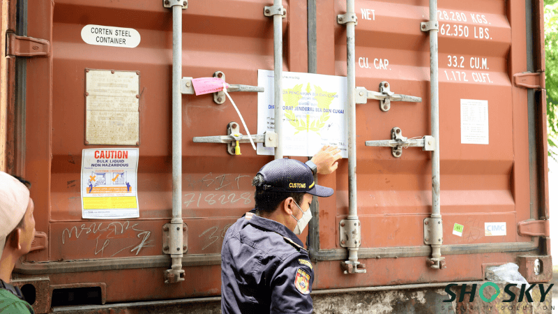 A customs officer inspecting and securing a shipping container door latch equipped with a security cable seal and official inspection documents.