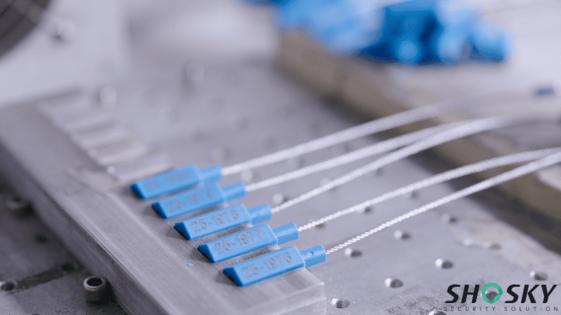 A row of blue plastic-body cable seals with laser-etched sequential serial numbers resting on a metal manufacturing fixture.