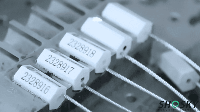 White hexagonal cable seal locks printed with sequential serial numbers arranged on a metal production line.