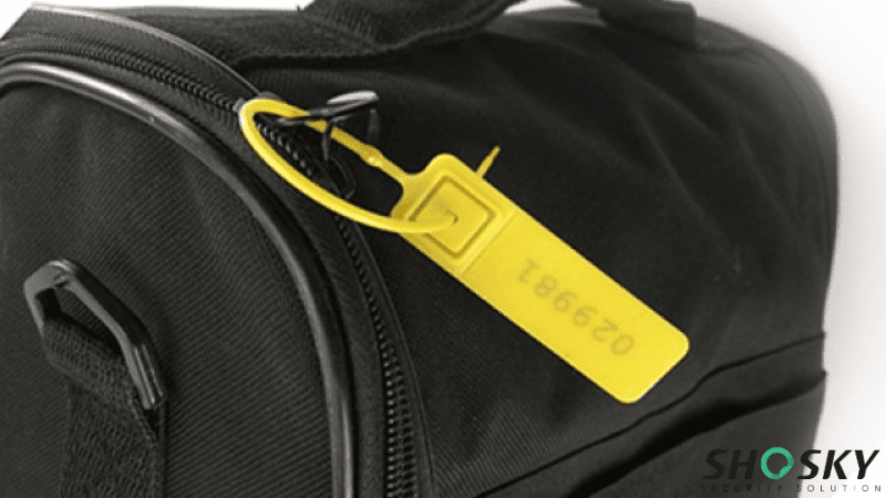 A bright yellow plastic bag seal with a printed serial number secured through the zipper of a black travel bag.