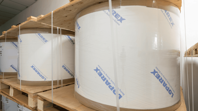 Large Loparex raw paper material rolls stacked on wooden pallets, made with SGS-certified materials for tamper-evident packaging production.