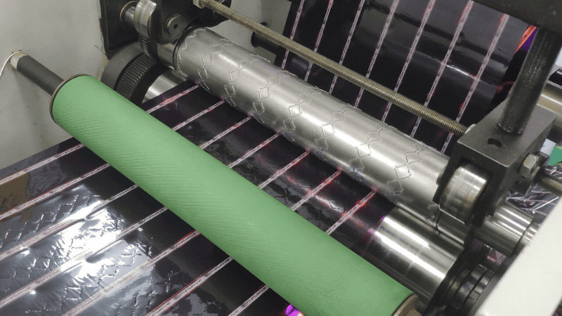 Automated machinery embossing pattern textures during the manufacturing of security bag sealing tape in a factory.