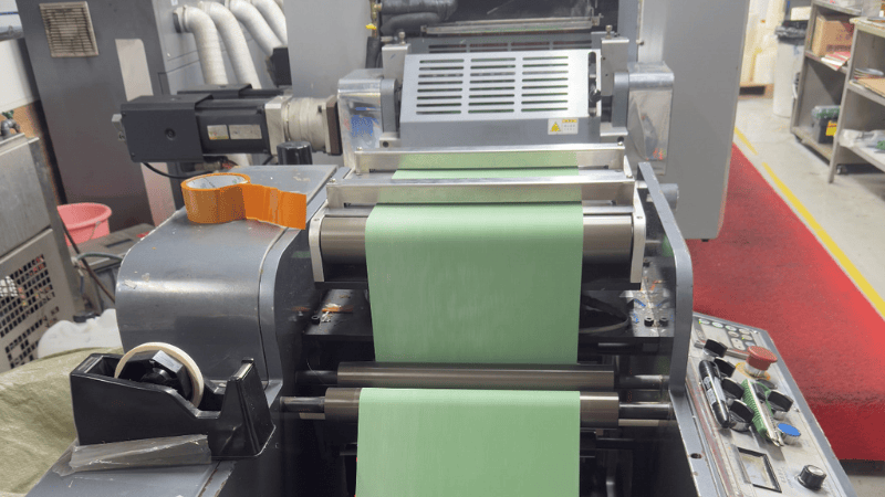 Industrial printing machine manufacturing green security label material roll in a factory setup.
