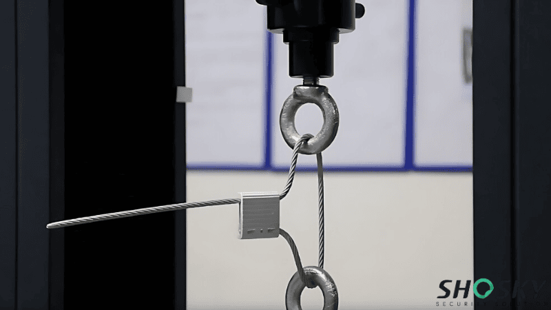 Industrial tensile testing machine performing a tensile strength and load capacity test on a metal cable security seal.