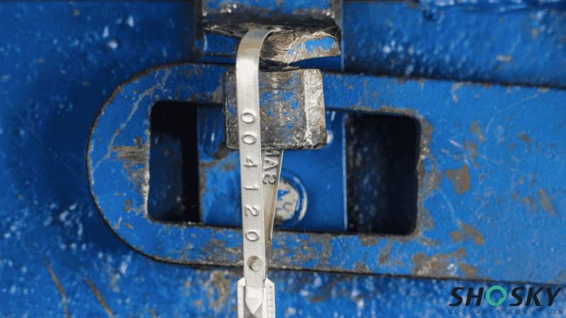A silver metal strap security seal stamped with a serial number secured to a blue container latch