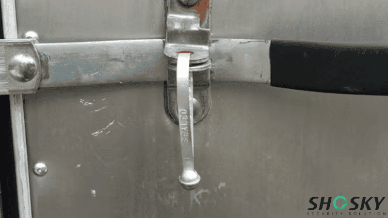 A silver metal strap seal stamped with the word "SEALED" locked onto the latch mechanism of a cargo door.