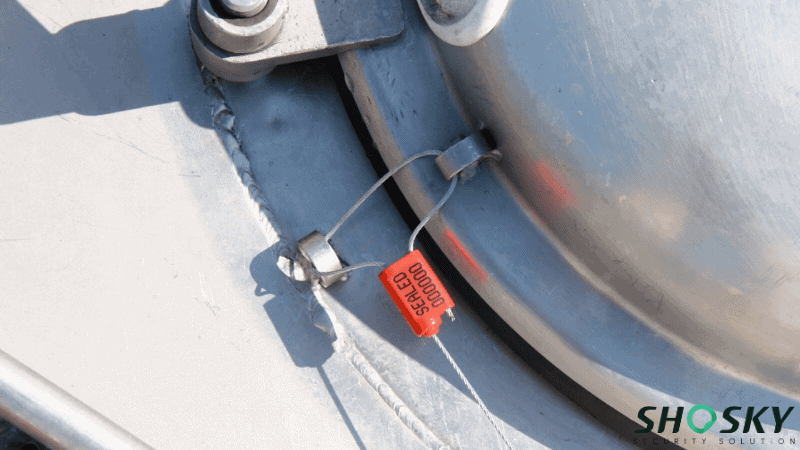 A red adjustable cable security seal with printed serial numbers attached to a metal tank hatch