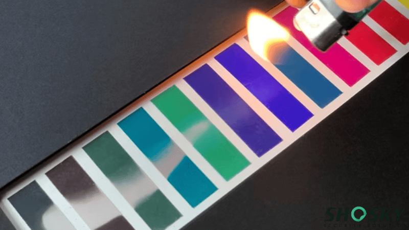 Heat-sensitive thermochromic security labels changing color under a lighter flame during a thermal anti-tampering test.